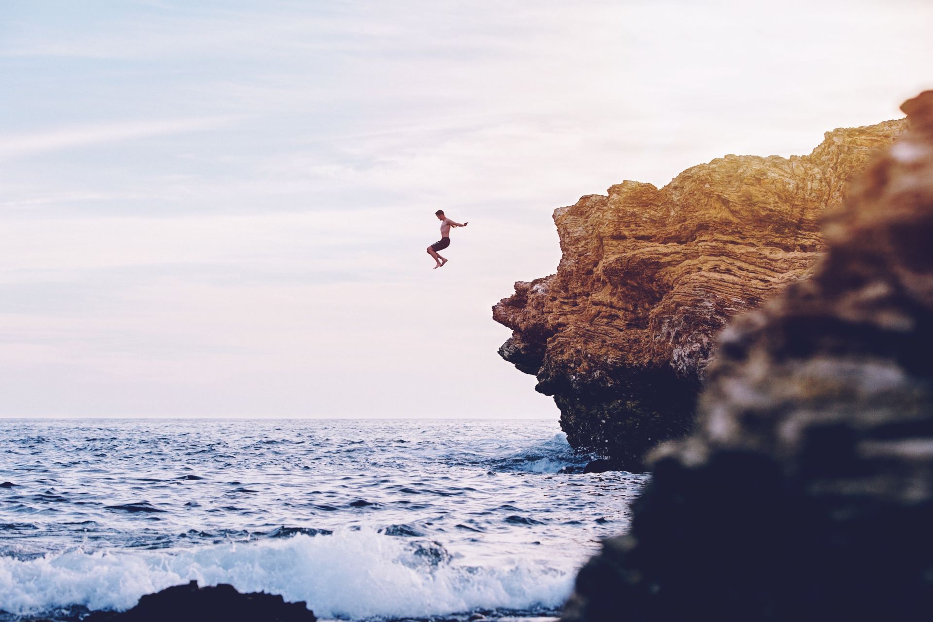Man jumping off a rocky cliff into the sea