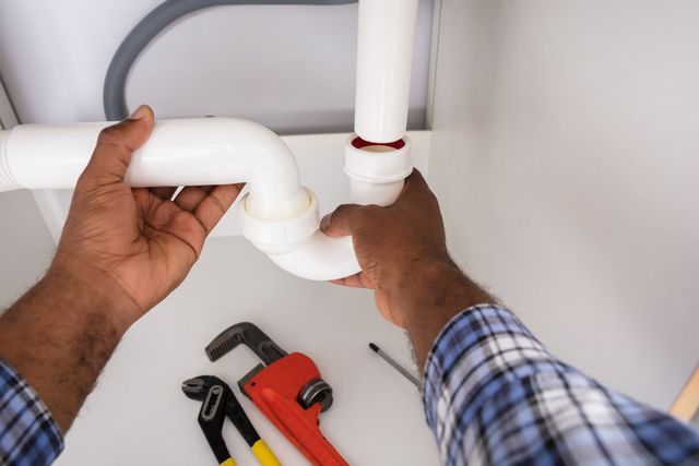 Plumber Fixing Water Pipe — Baltimore, MD — Geo's Plumbing Services A plumber is fixing a pipe under a sink.