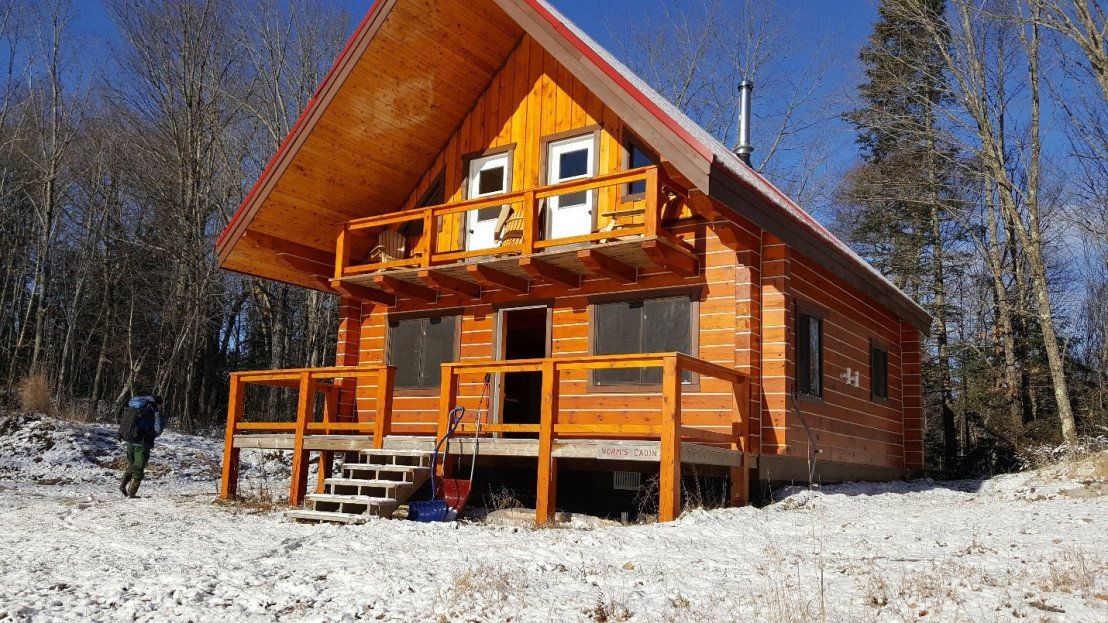 Slider image showing what Norm's Cabin looks like now. It's a 1.5 story cabin featuring upper and lower decks.
