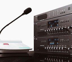 A microphone is sitting next to a stack of speakers on a table.