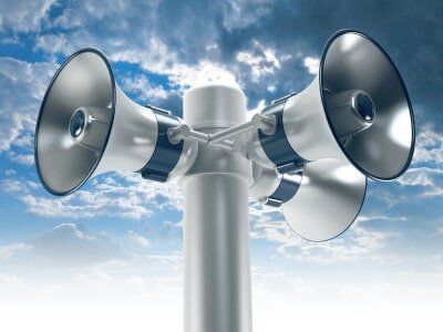 Three speakers are attached to a pole with a blue sky in the background.
