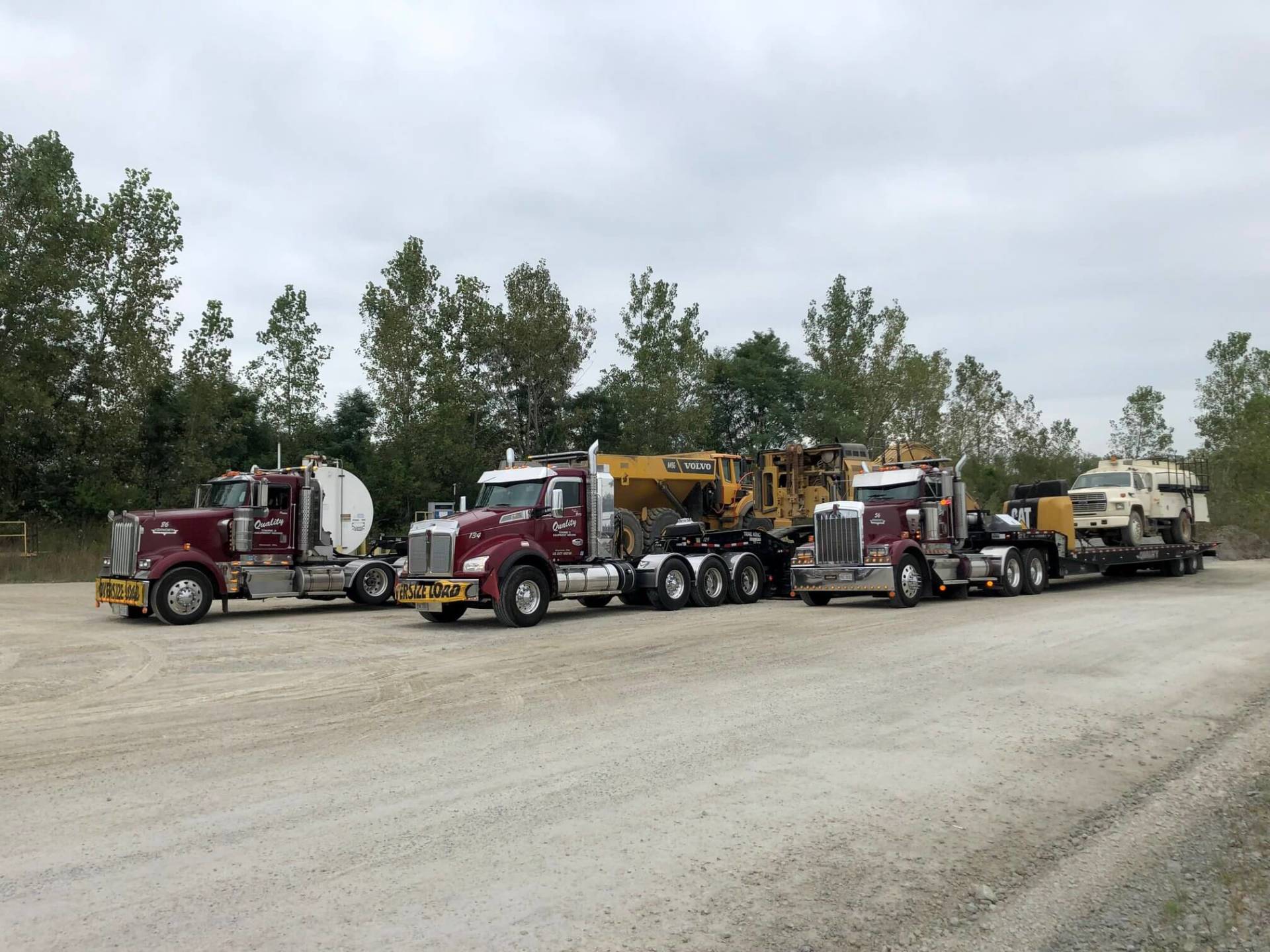 A row of semi trucks are parked on a dirt road.
