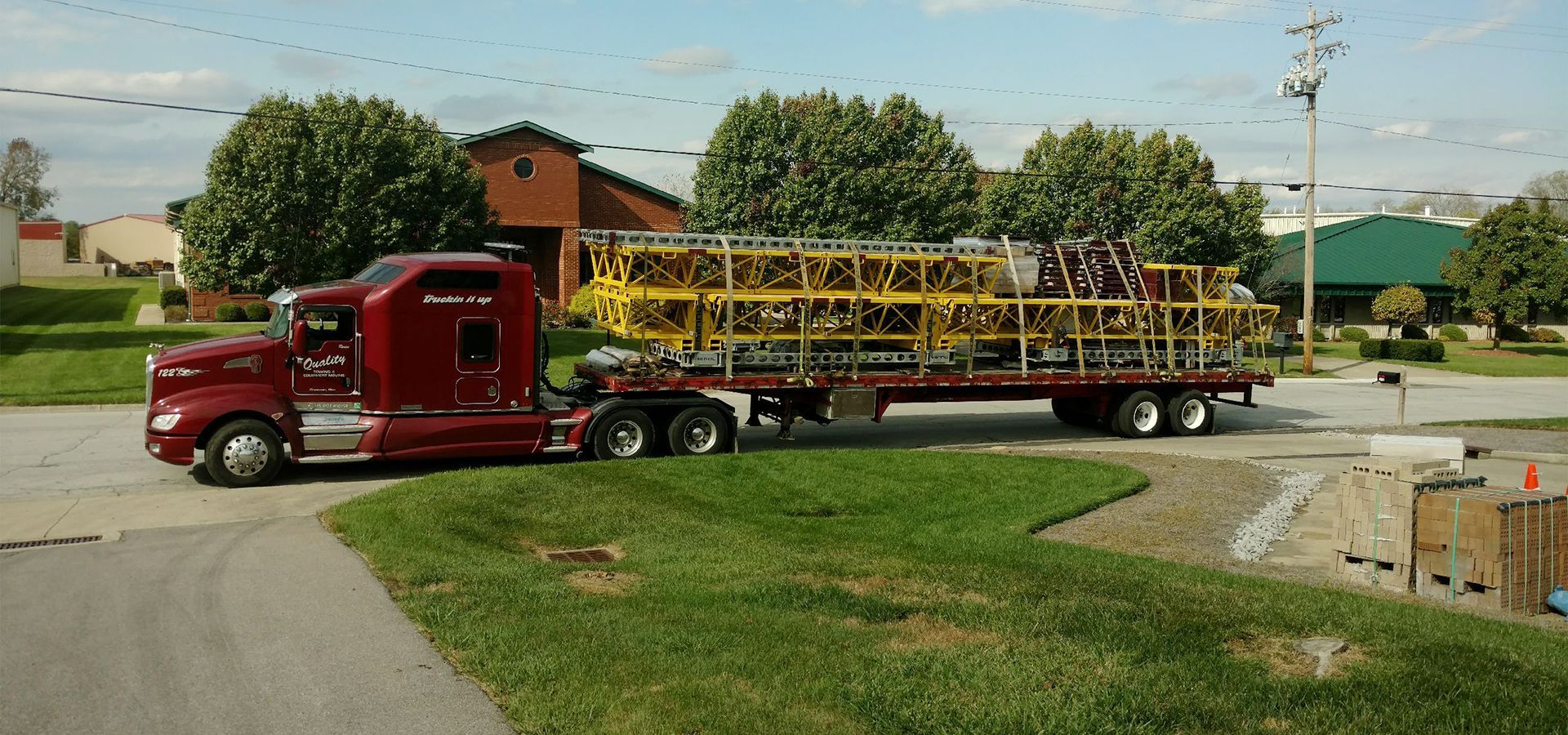 A red semi truck is carrying a yellow ladder on a flatbed trailer.