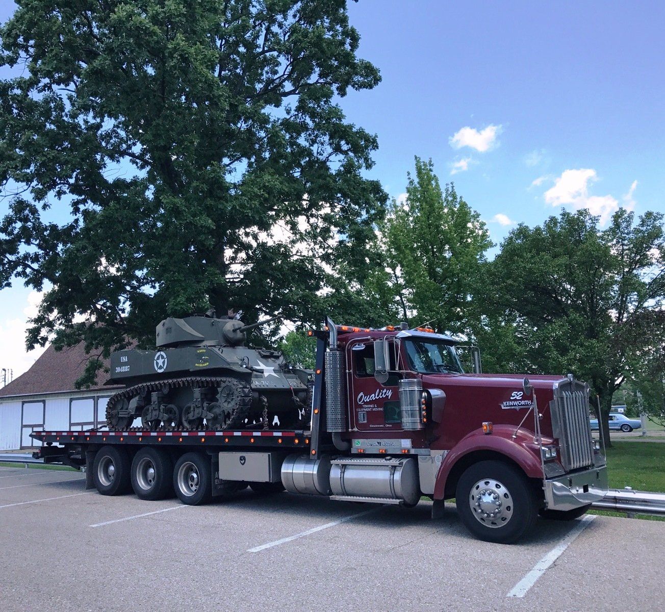 A red tow truck with a tank on the back is parked in a parking lot