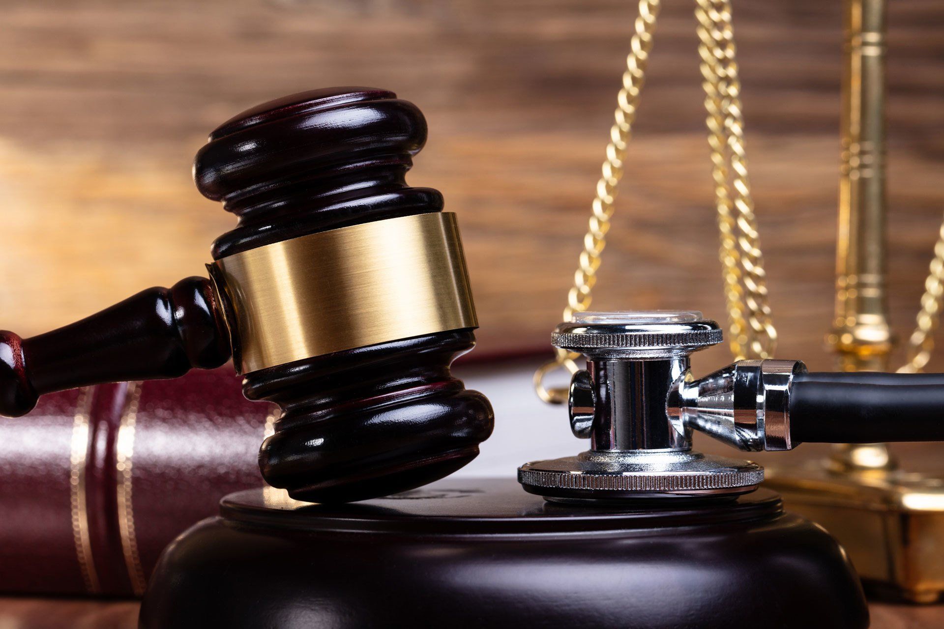 Gavel and stethoscope on a stand with legal book and scales in the background, representing medical law.