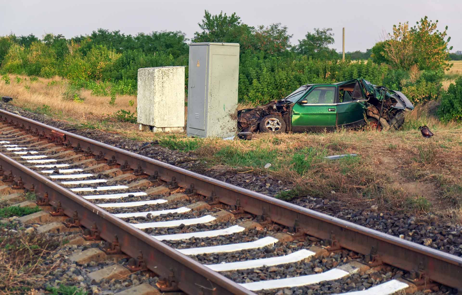 A green car severely damaged near a train track after apparent crash. A green car severely damaged near a train track after apparent crash.