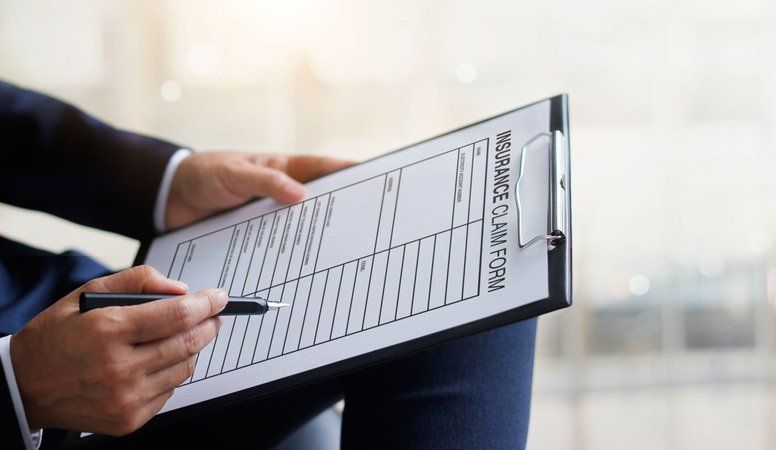 Person in suit filling out an insurance claim form with a pen.