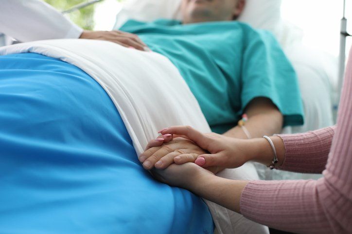 Person in hospital bed holds hands with another person.