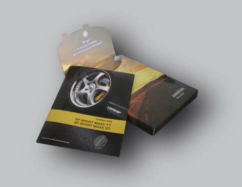 Opuscolo in una scatola brandizzata; raffigurante una ruota di automobile, dettagli neri e gialli e confezione aperta.