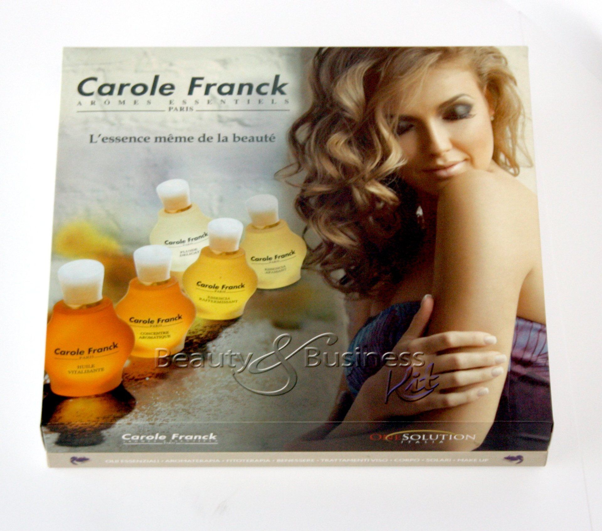 Scatola di cosmetici Carole Franck con flaconi e una donna con effetto soft focus; colori crema, arancione e oro.
