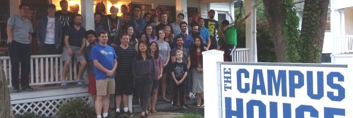 A group of people are standing in front of a sign that says campus house.