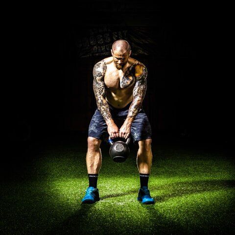 A man is squatting down while holding a kettlebell in his hands