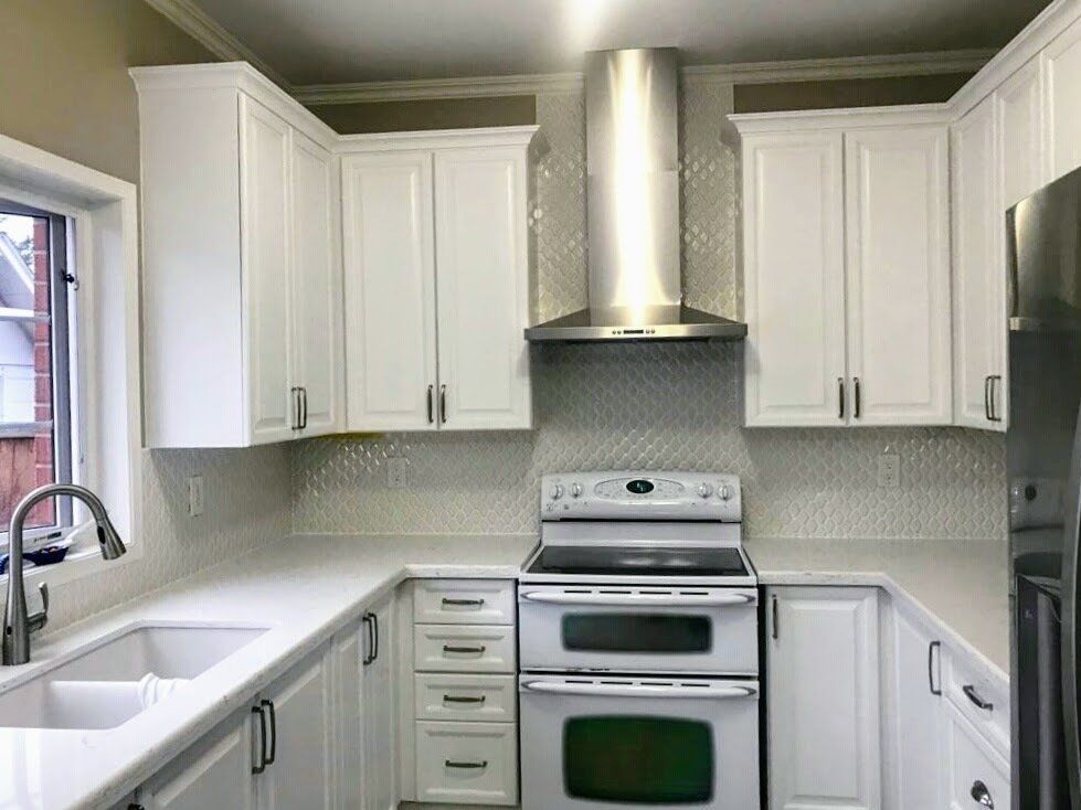 A kitchen with white cabinets , a stove , a sink , and a refrigerator.