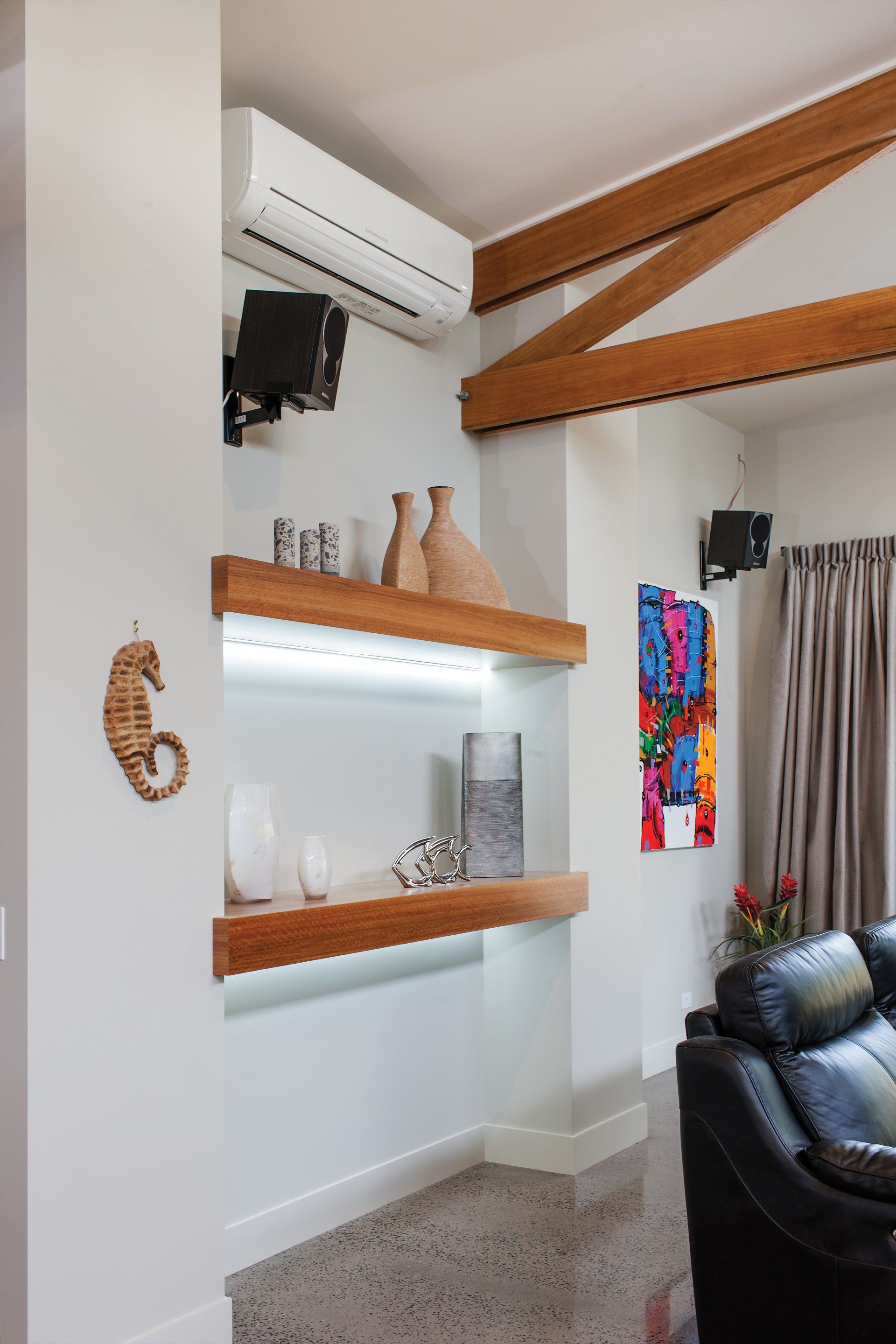 A living room with a couch , shelves , and a seahorse on the wall.