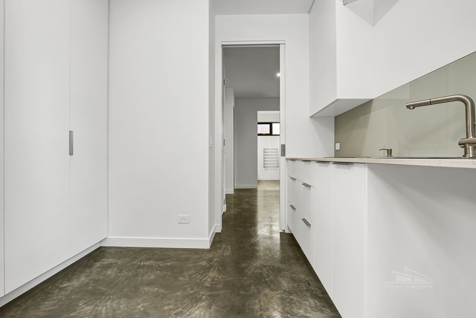 An empty kitchen with white cabinets and a sink.