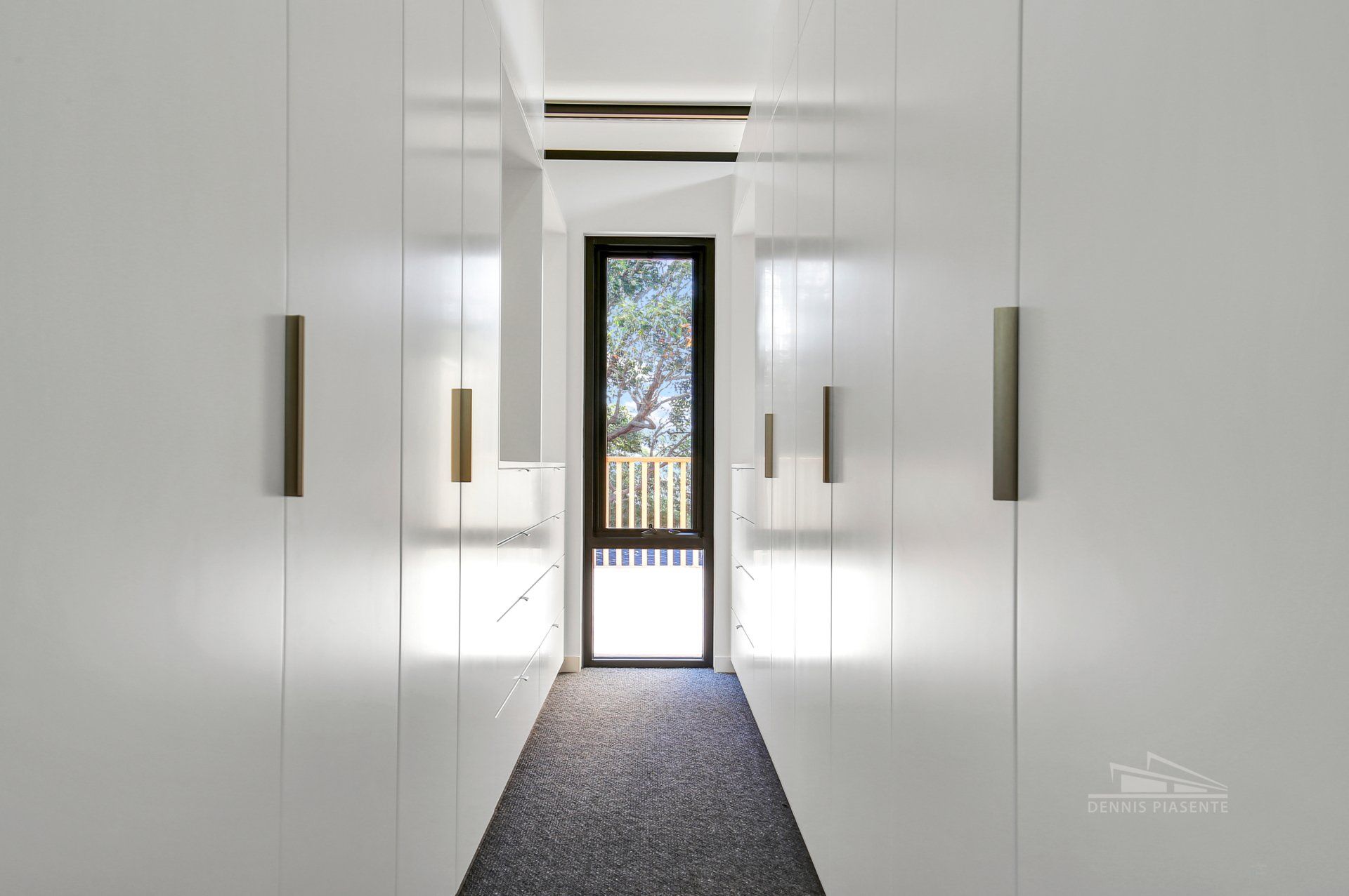 A long hallway with white cabinets and a window.