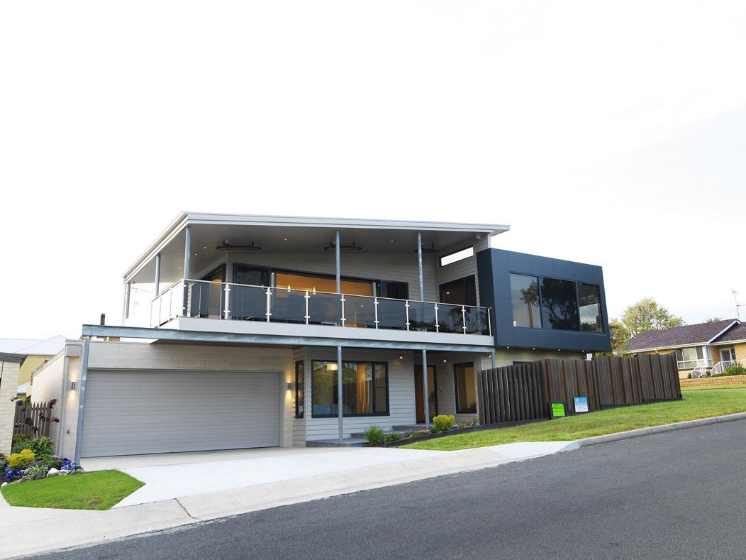 A large house with a garage and a balcony is sitting on the side of a road.