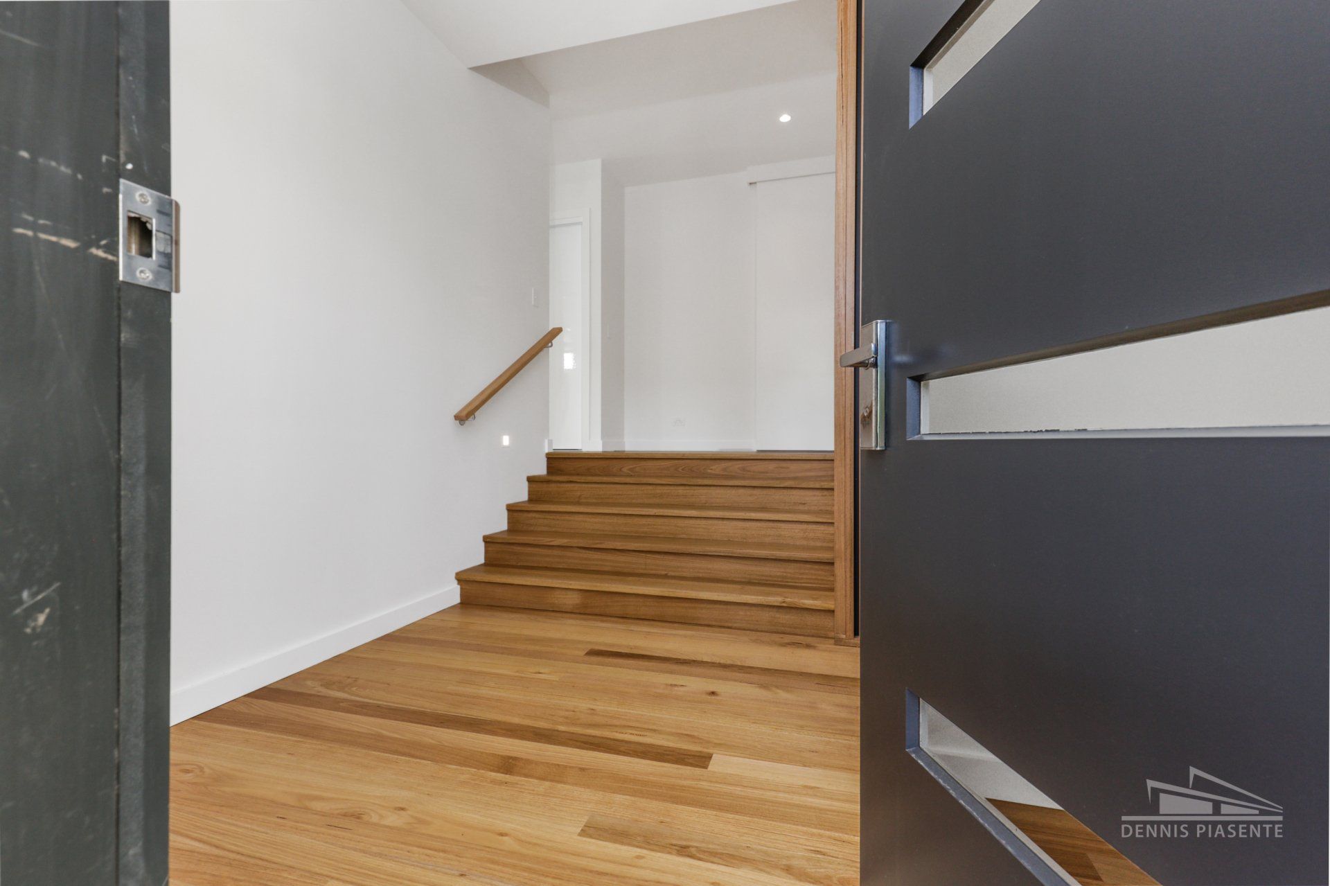 A black door is open to a hallway with wooden stairs