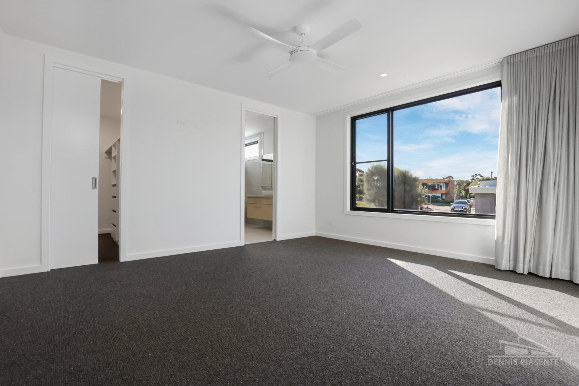 An empty bedroom with a large window and a ceiling fan