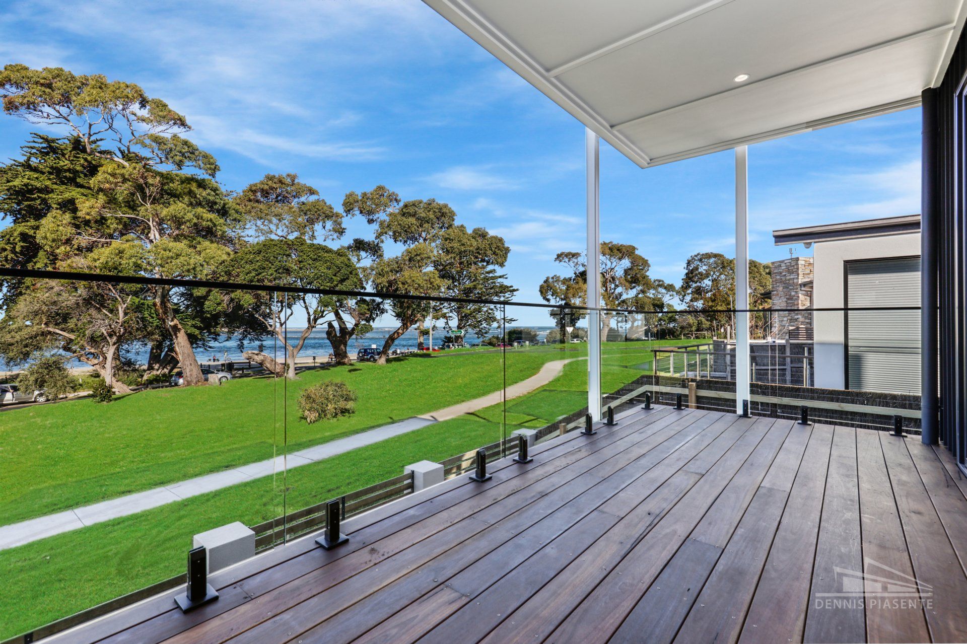 A wooden deck with a glass railing overlooking a grassy field