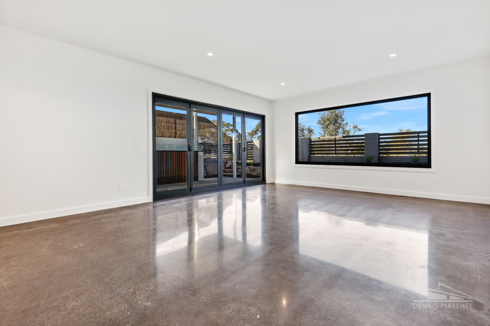 An empty living room with a large window and sliding glass doors.