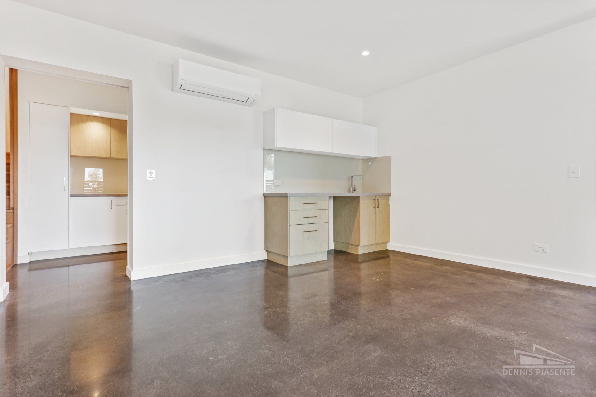 An empty living room with a kitchen in the background