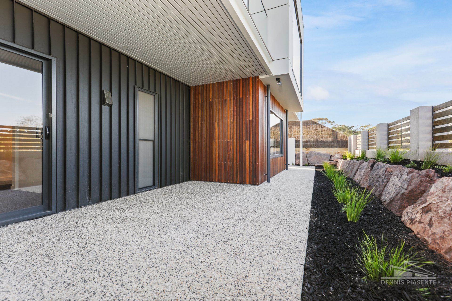 A patio with gravel in front of a house with a black siding.
