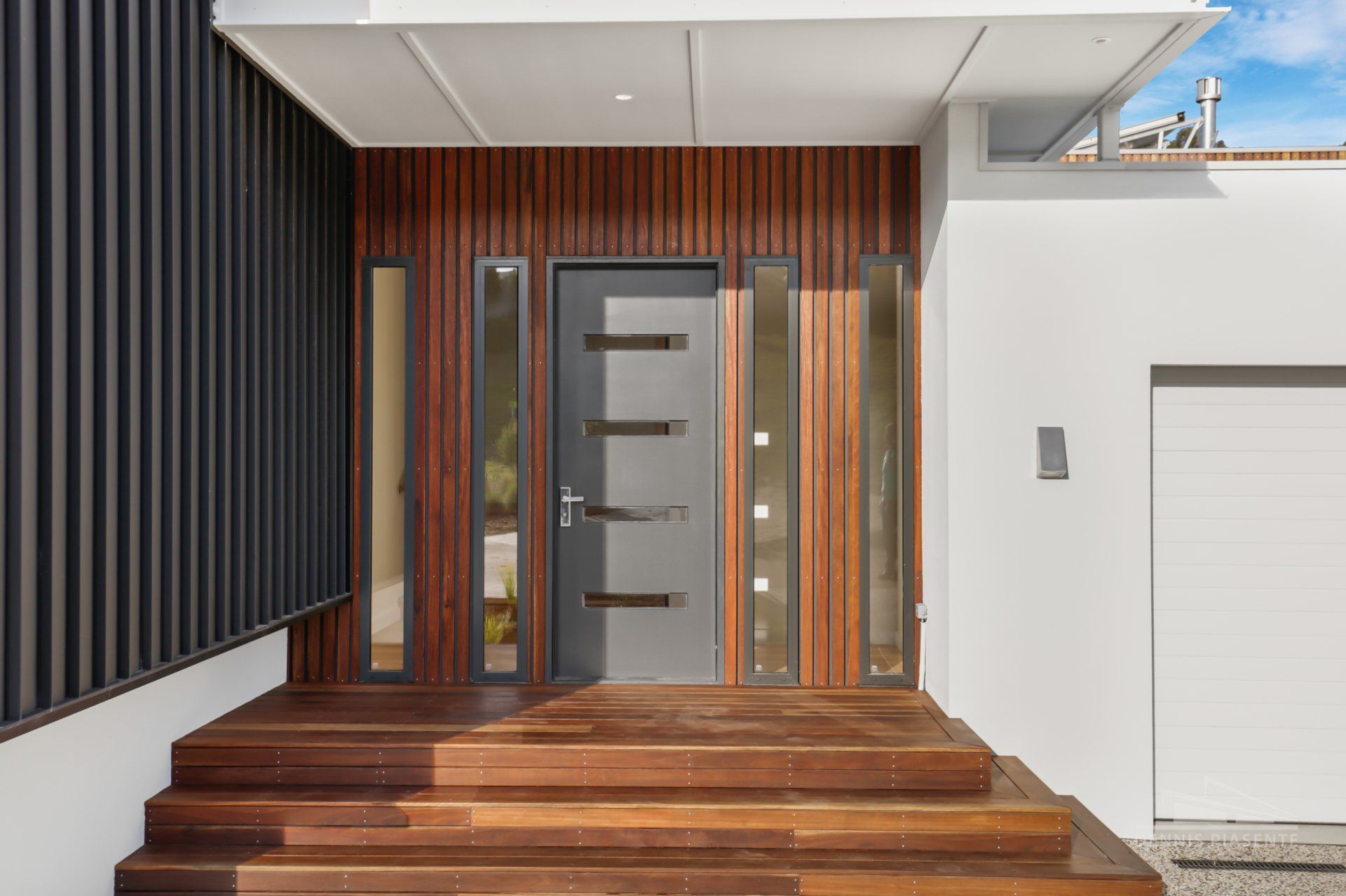 The front door of a modern house with wooden steps and a wooden porch.