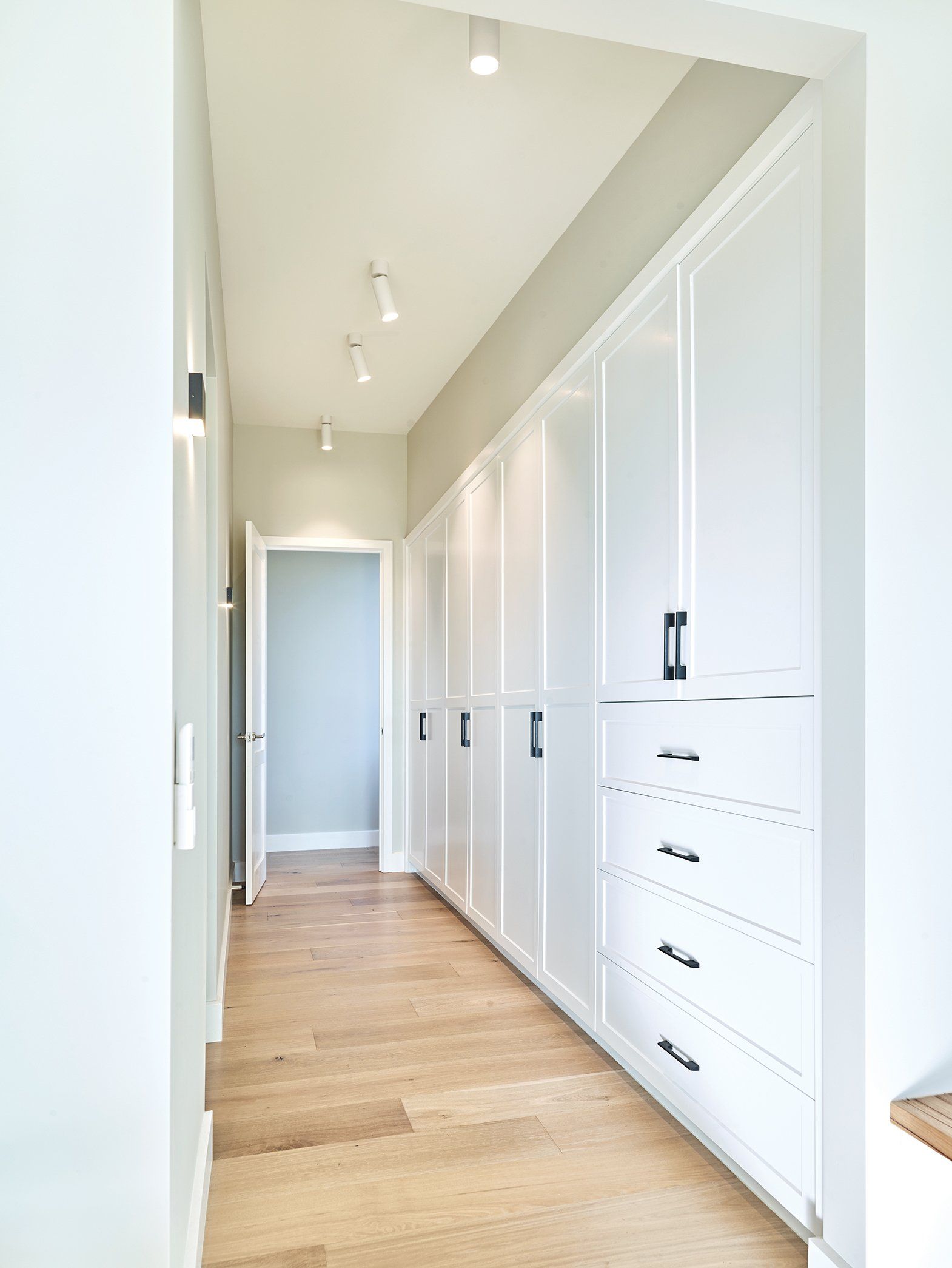 A long hallway with white cabinets and drawers and wooden floors.