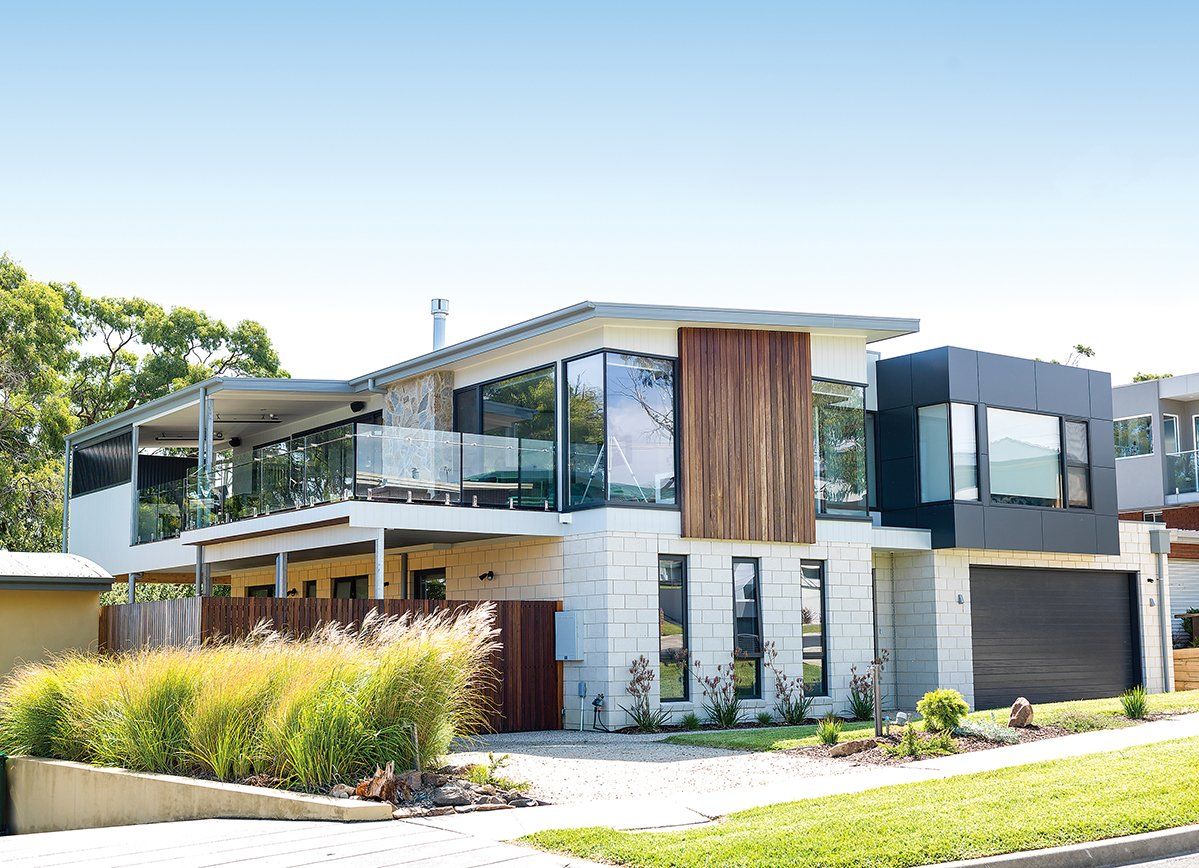 A large modern house with a lot of windows is sitting on top of a lush green hillside.