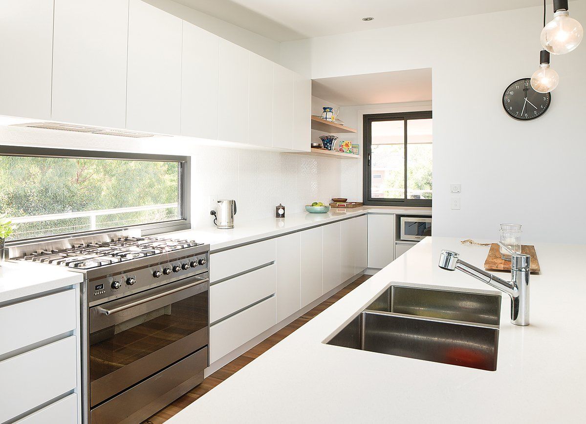 A kitchen with white cabinets , a stove , a sink , and a window.