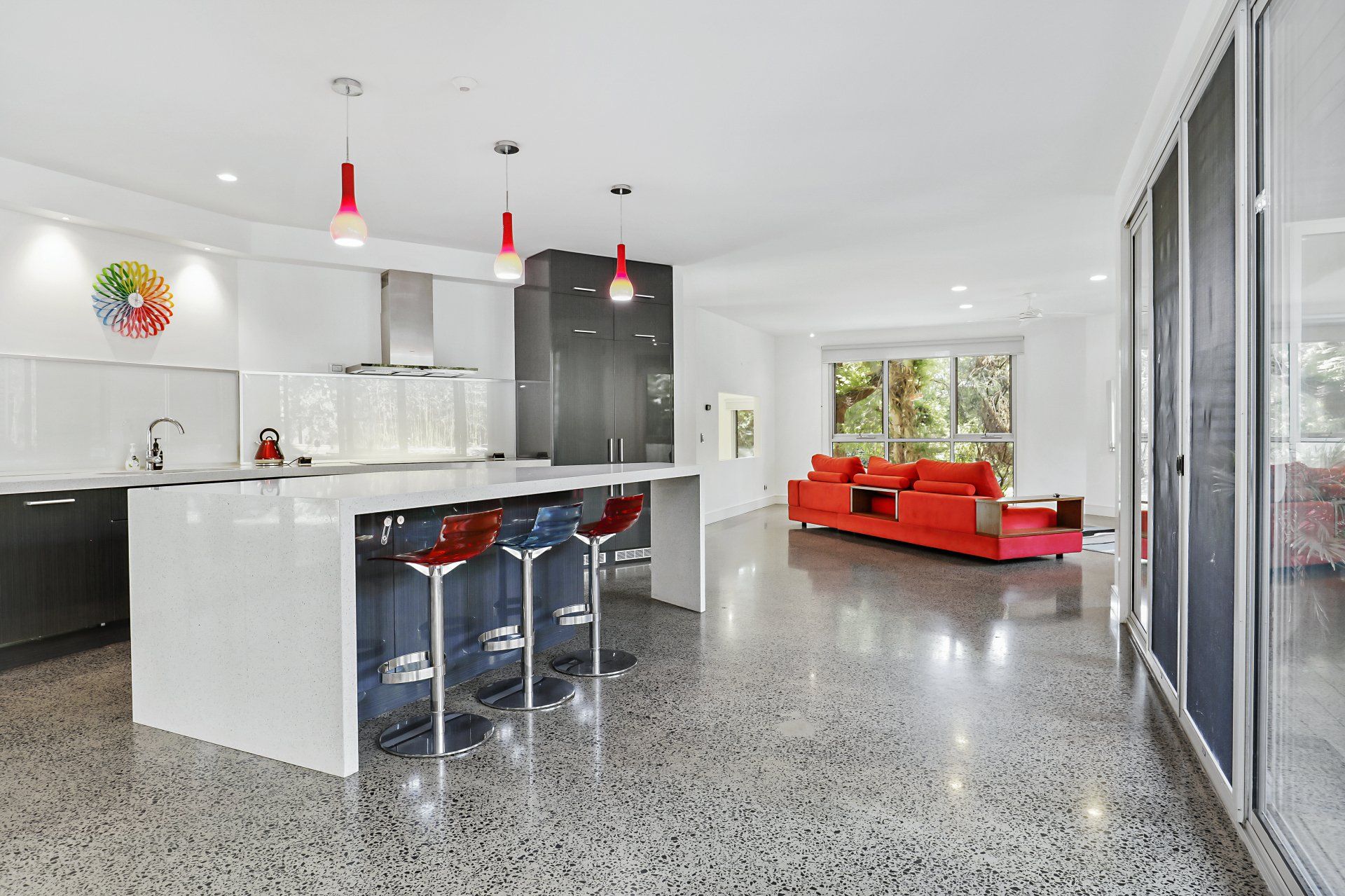 A kitchen with a large island and stools and a living room with a red couch.