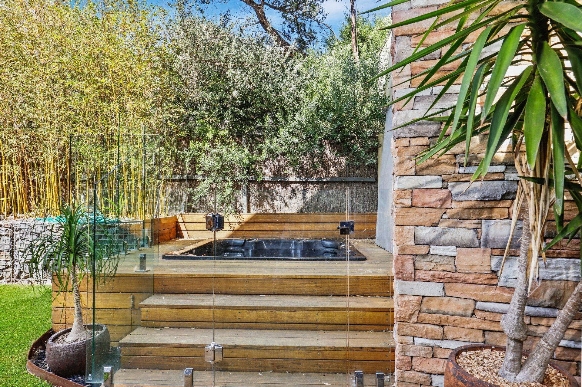A hot tub is sitting on top of a wooden deck next to a stone wall.