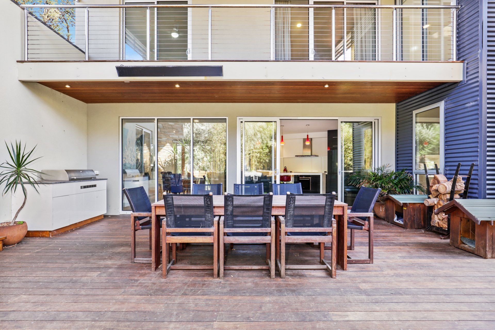 There is a large table and chairs on the deck of a house.
