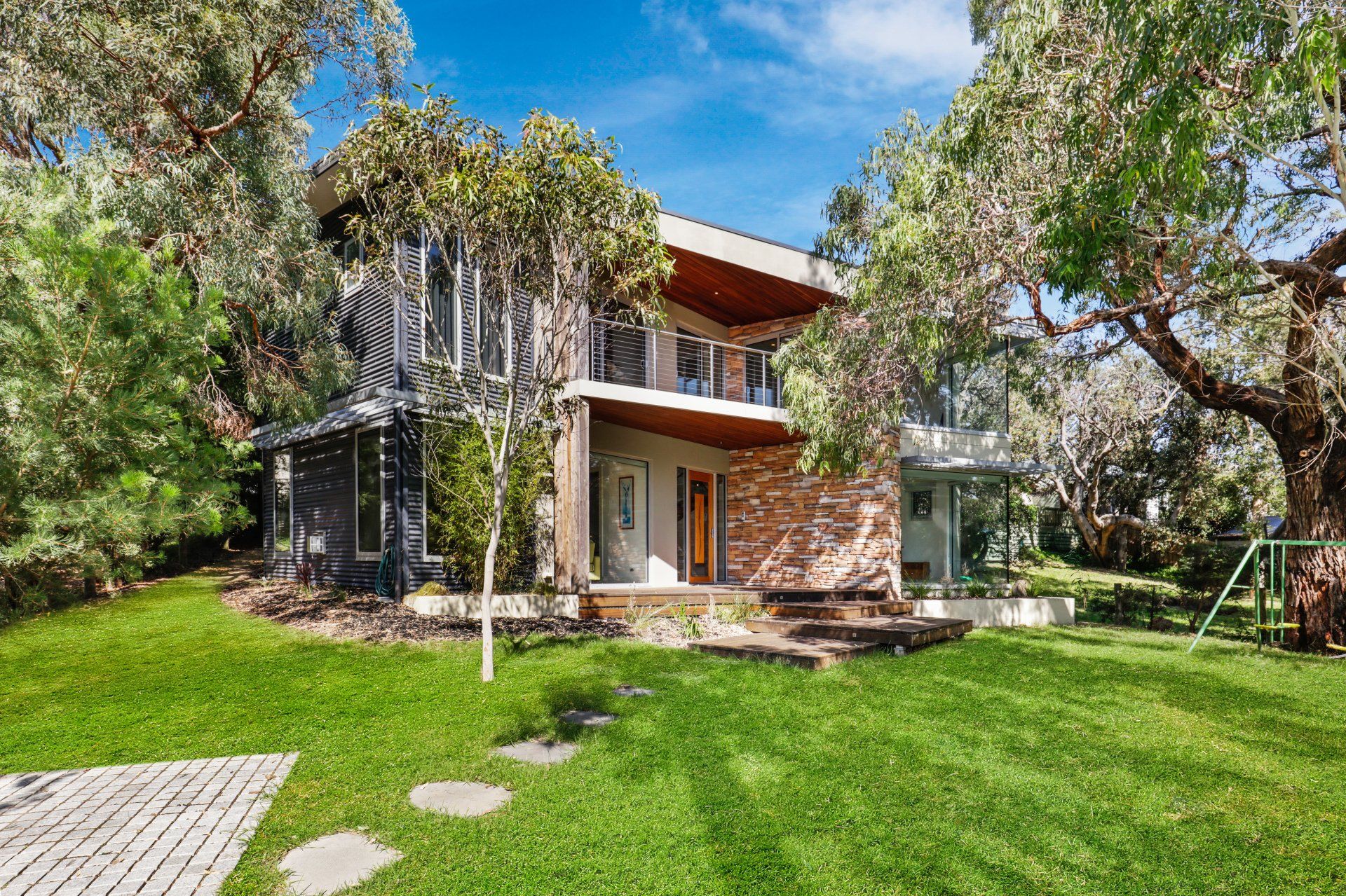 A modern house with a large lawn and trees in front of it.