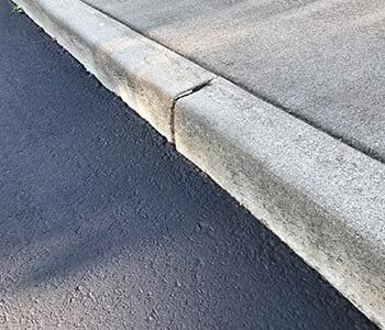 Concrete curb next to asphalt road. A crack is visible where two sections meet.