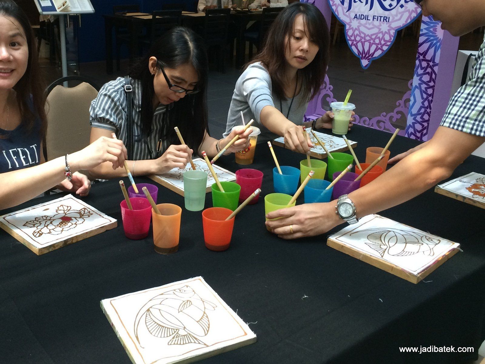 People painting on wooden plaques, using colorful paints and brushes at a table.