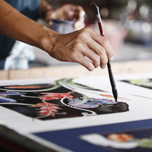 Person painting vibrant floral design on fabric with brush.