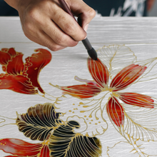 Hand painting a floral design with red and gold on white fabric.