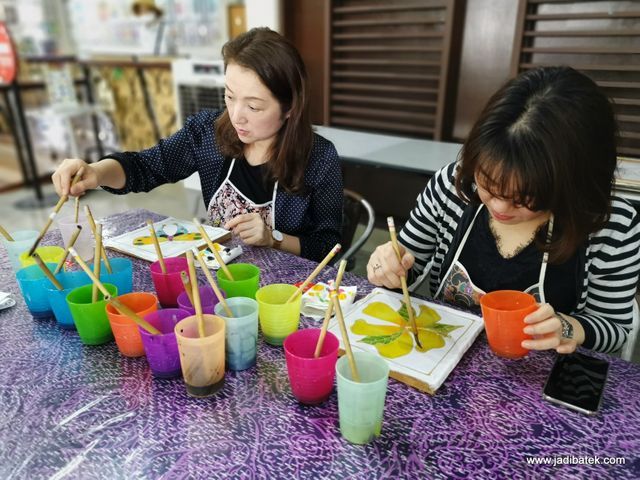 Two women painting with brushes at a table, colorful cups of paint, indoors.