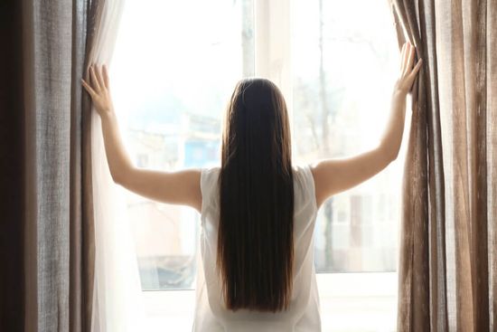 ragazza apre tende per guardare alla finestra
