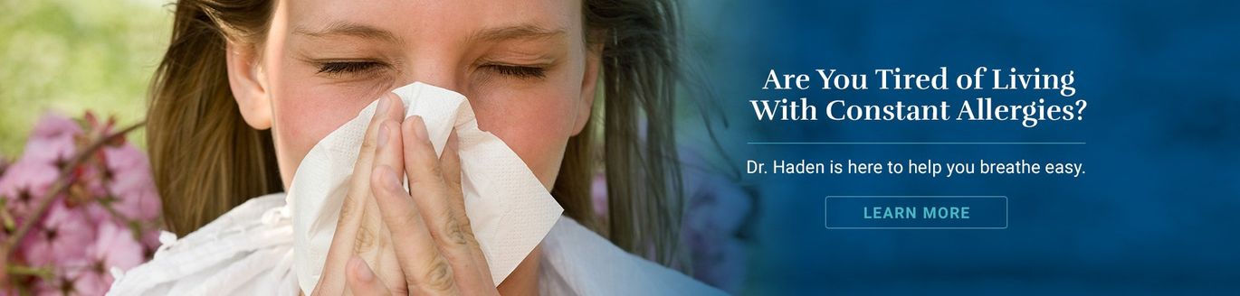 Woman with closed eyes blowing her nose, text: Are you tired of living with constant allergies? Learn More.