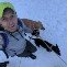 Person in a bright hat and jacket, climbing snowy slope with an ice axe.