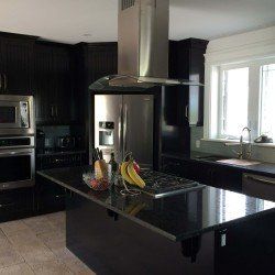 A kitchen with black cabinets , stainless steel appliances , a stove top oven and a refrigerator.