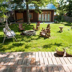 A backyard with a fire pit , chairs , a swing and a wooden deck.