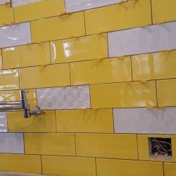 A bathroom wall with yellow and white tiles and a faucet.