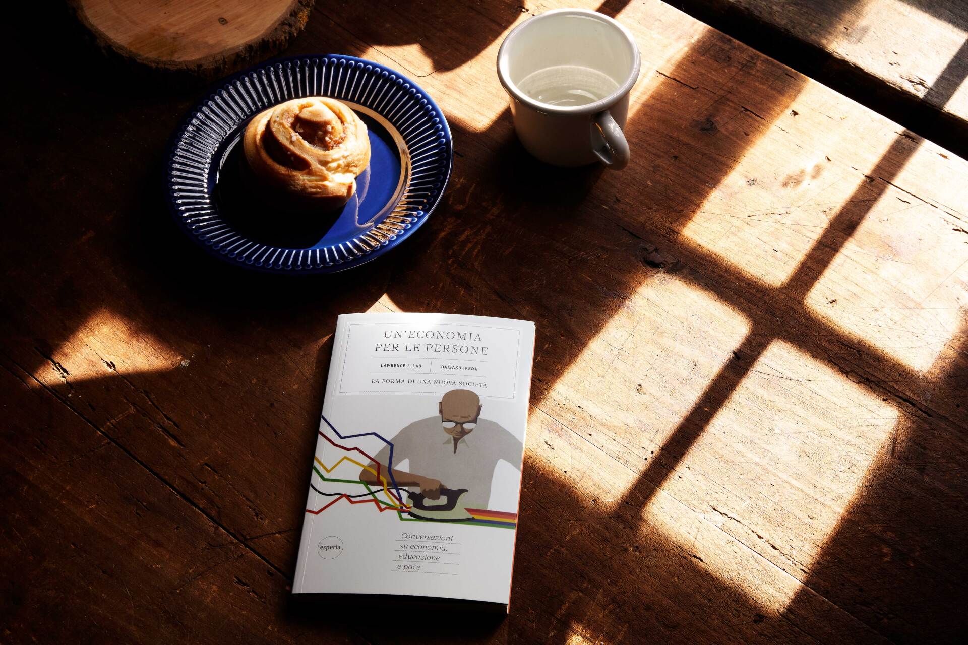 Un libro è appoggiato su un tavolo di legno, accanto a un piatto di cibo e a una tazza d'acqua.