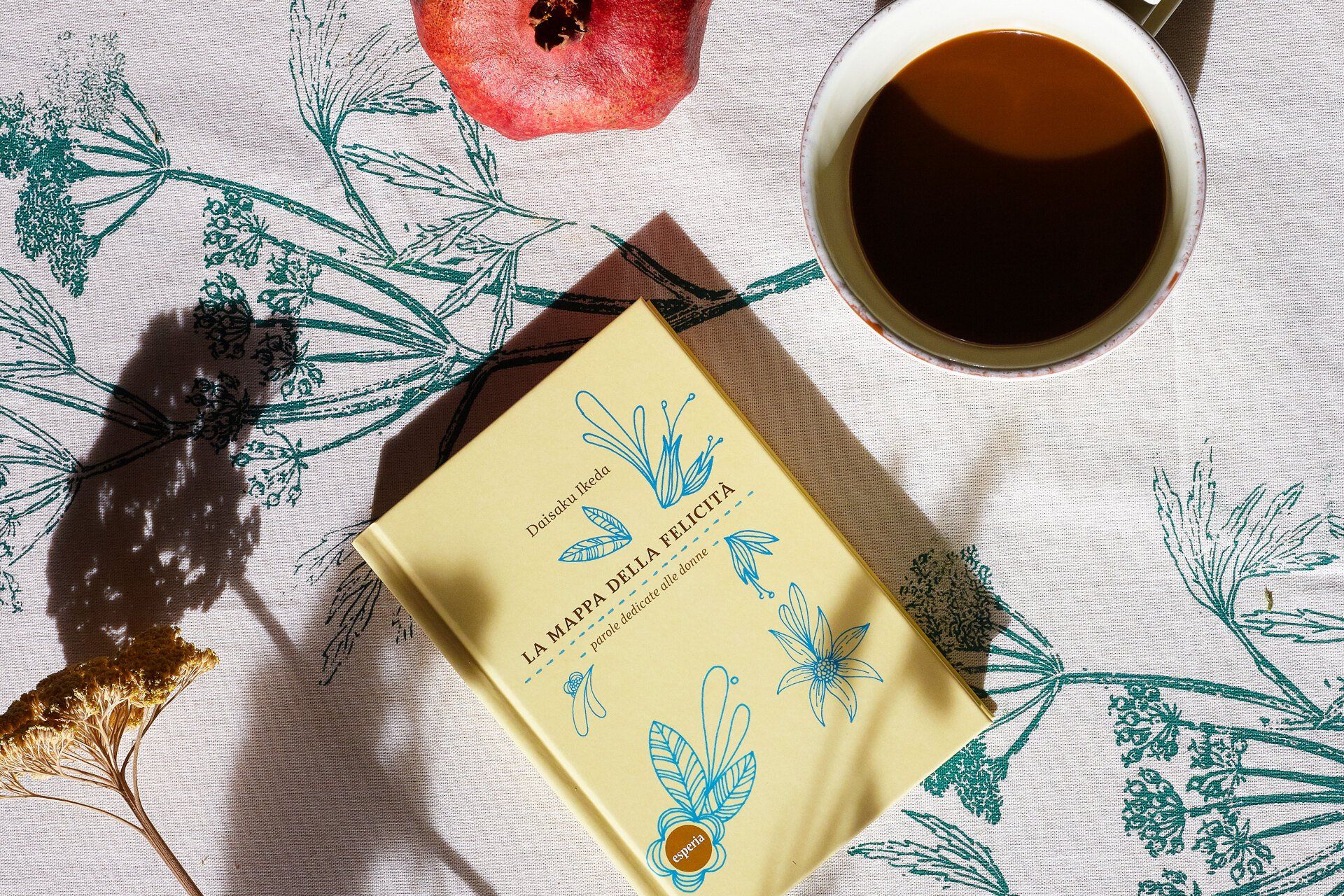 Un libro è appoggiato su un tavolo accanto a una tazza di caffè e un melograno.