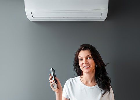 Woman holding a remote under a wall-mounted air conditioner against a gray wall