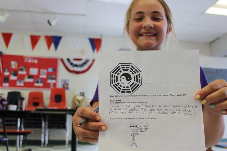 girl holding up piece of paper with drawing on it to the camera